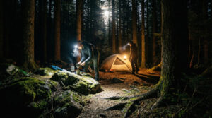 Best headlamps for hiking & camping lighting a forest trail at night with hikers setting up camp