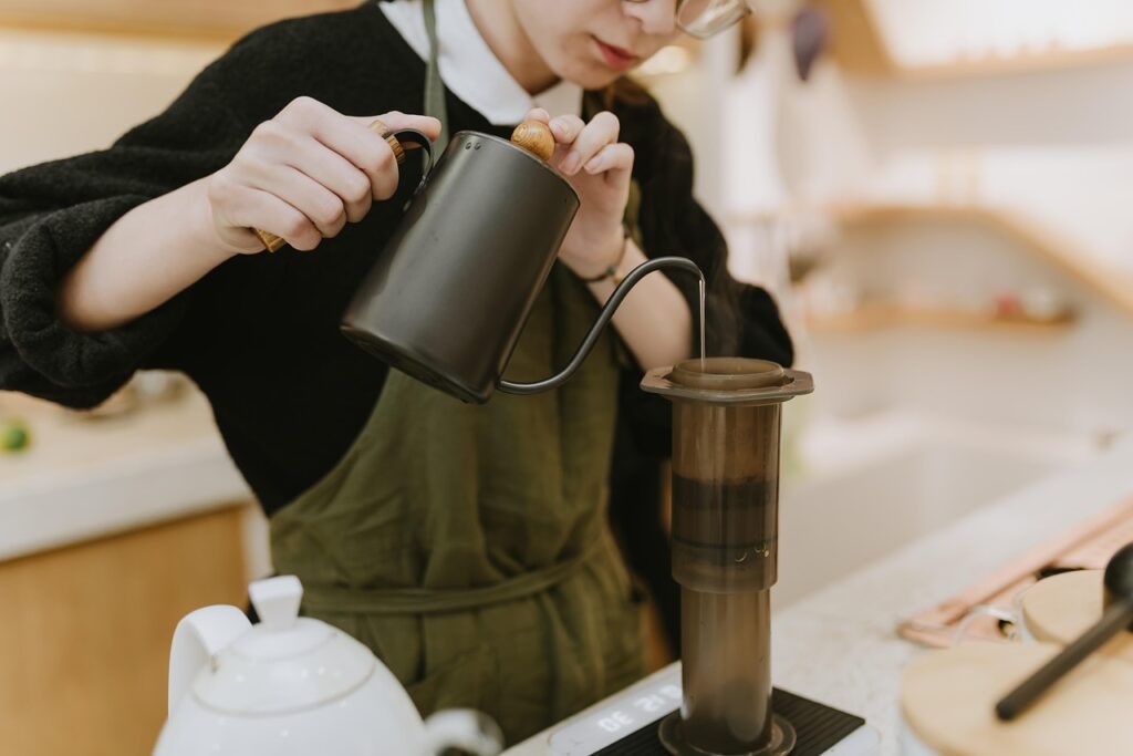A camper wearing heavy gloves pouring steaming hot coffee from a vacuum-insulated bottle outdoors.